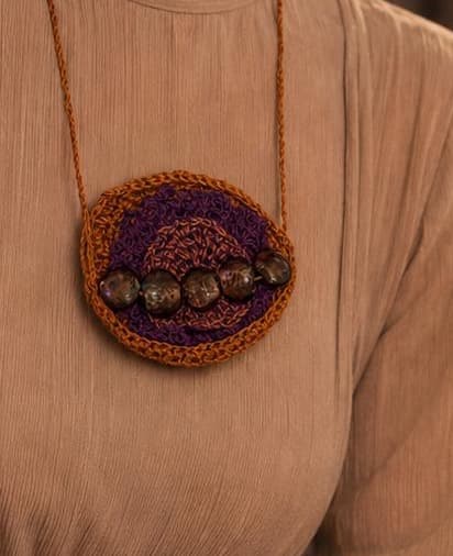 Colar Frutos da Noite: medalhão circular de crochê ferrugem e laranja com centro roxo e fileira de contas escuras iridescentes